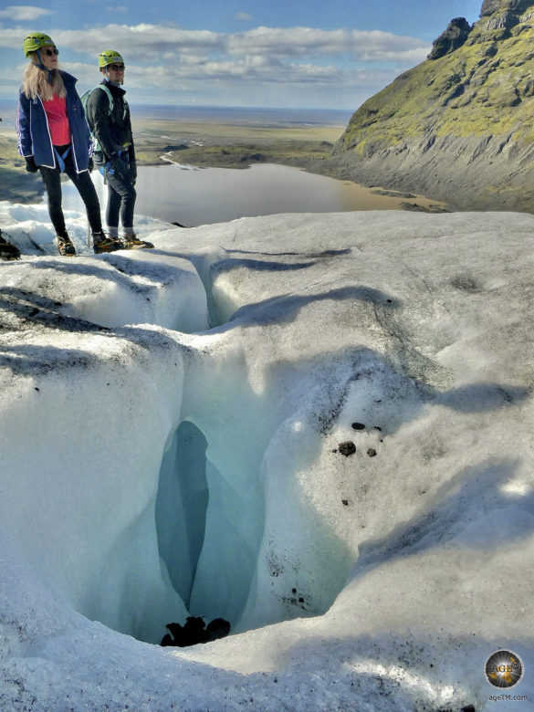 Zwei Wanderer auf zerklüftetem Eis vor einer idyllischen Landschaft.