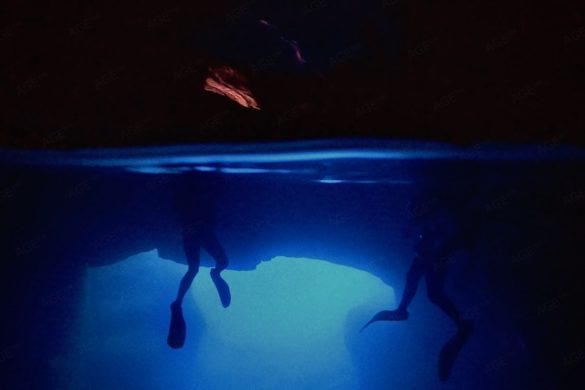 Unterwasserfoto zeigt 2 Höhlentaucher halb unter und über Wasser. Höhlentauchen in der Cathedral Cave Insel Gozo Malta. Tauchen Aktivurlaub auf den Inseln Malta Gozo Camino Europa