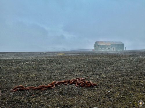 Eisenkette und Flugzeughangar auf Deception Island im Schneeregen.