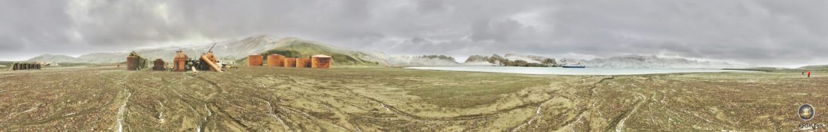 Panorama der Whalers Bay. Vulkanische Ebene, rostrote Tanks und weiße Gebirge im Kontrast.