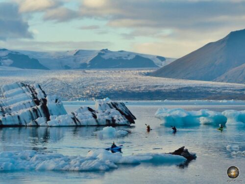 Kajakfahrer zwischen Eisbergen mit schwarzen Aschestreifen in Island auf dem Gletschersee Jökulsárlón in Island