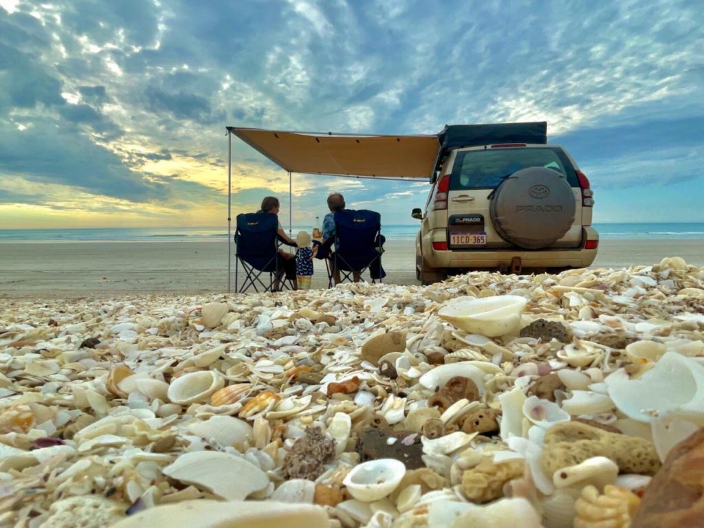 Toyota Prado Camper Familie sitzt unter dem Sonnensegel am Strand mit Muscheln