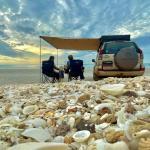 Toyota Prado Camper Familie sitzt unter dem Sonnensegel am Strand mit Muscheln